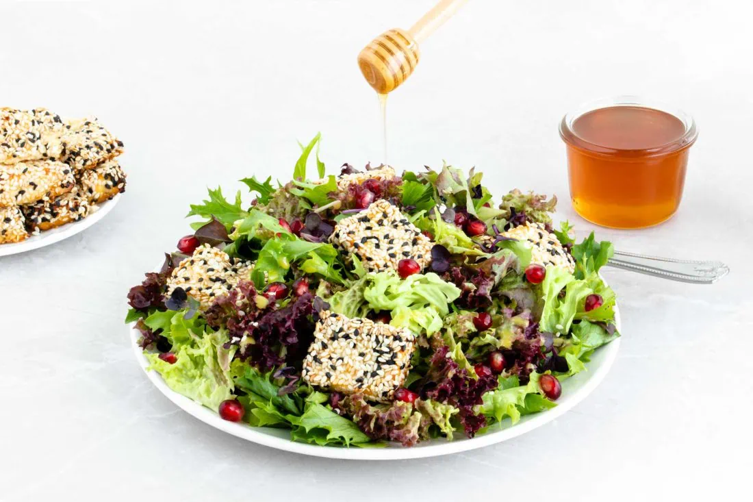 Salat mit Feta im Honig-Sesam Mantel-2 Salat mit Feta im Honig-Sesam Mantel wird mit einem Honiglöffel mit flüssigem Honig beträufelt.