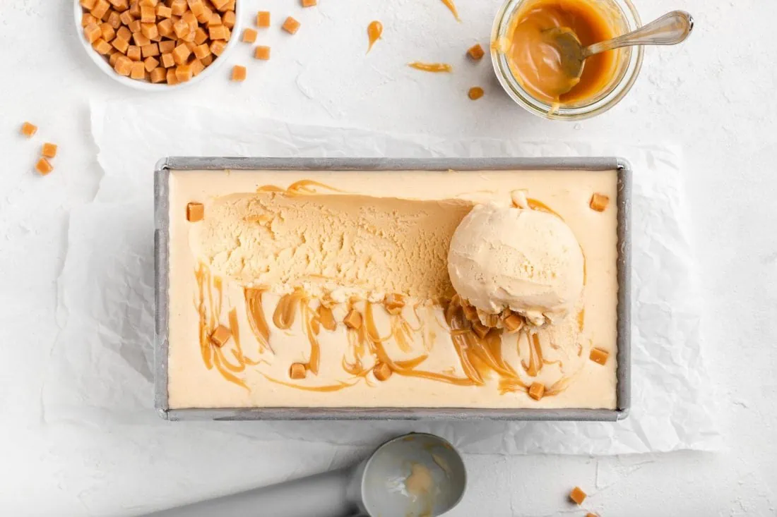 Cremiges Salted Caramel Eis aus der Eismaschine in eienr rechteckigen Form garniert mit kleinen Karamellstücken und Karamellsoße.