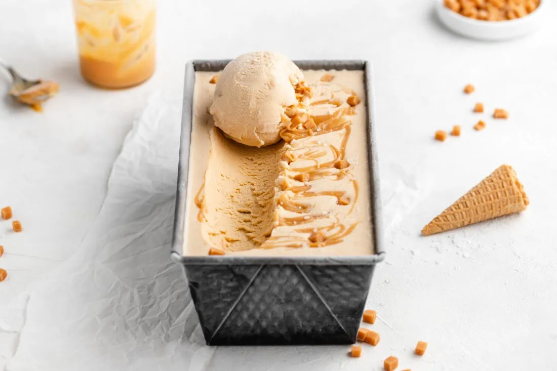Selbstgemachtes Salted Caramel Eis aus der Eismaschine. Auf der mit Eis gefüllten Form liegt eine Eiskugel.