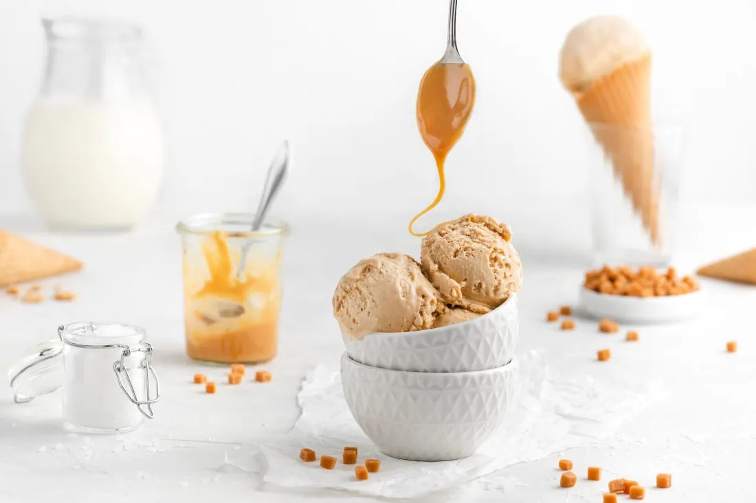 Mehrere Kugeln Salted Caramel Eis aus der Eismaschine werden mit einem Löffel mit der selbstgemachten Karamellsauce beträufelt.
