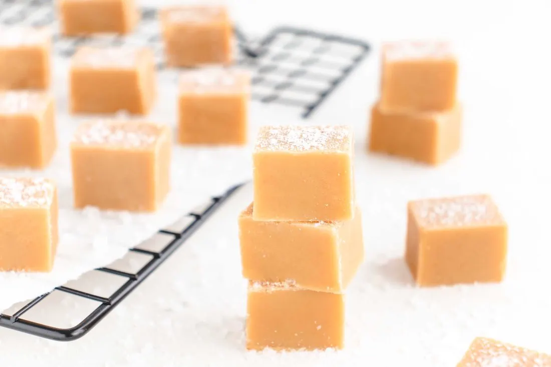 Auf einem schwarzen Gitter liegen mehrere mit Meersalz bestreute Würfel des Salted Caramel Fudge.