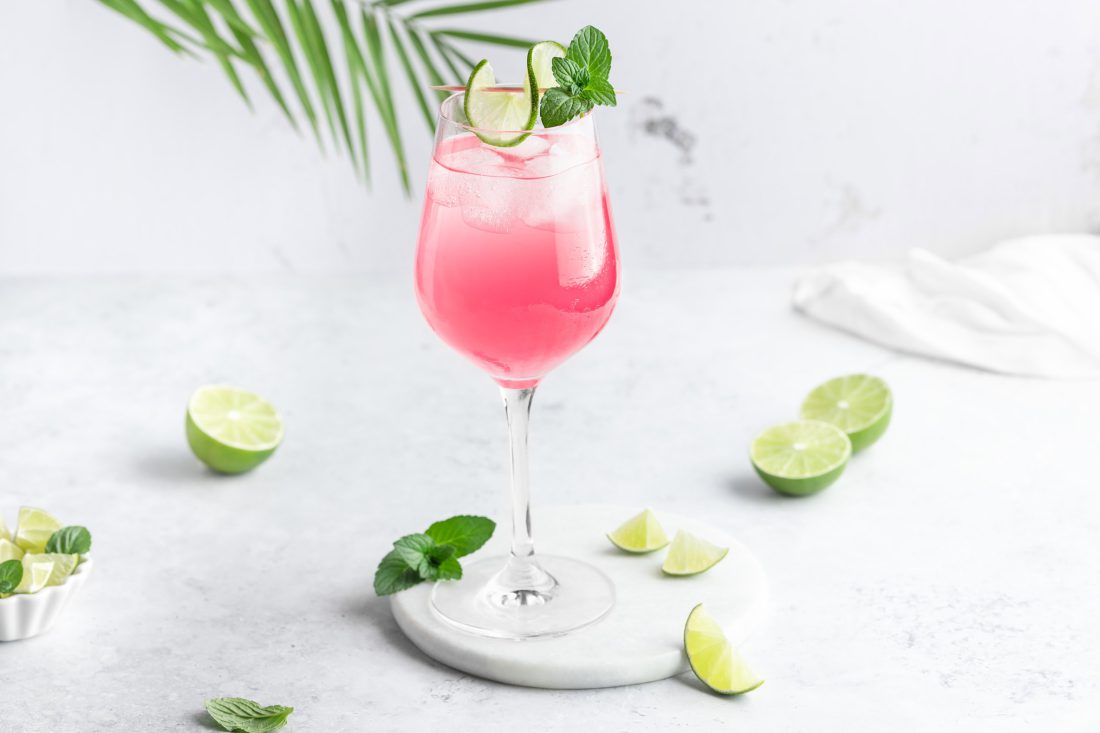 Sarti-Spritz-3 Ein rosafarbener Aperitif, der original Sarti Rosa, in einem Weinglas mit einer Limettenscheibe und frischer Minze garniert.