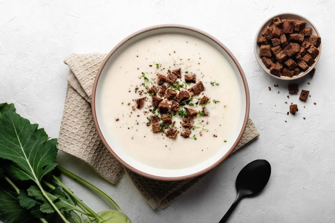 Kohlrabisuppe mit feinen Stücken knusprigen Vollkornbrot und frischer Kresse. Daneben steht ein Schälchen mit weiteren Croûtons.