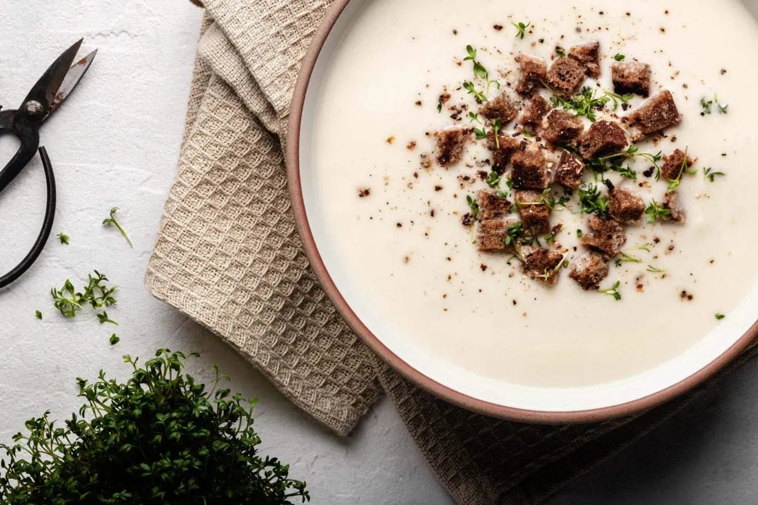 Schnelle Kohlrabisuppe mit Croûtons und frischer Kresse in einem Suppenteller. Neben dem Teller steht eine Schale mit Kresse.
