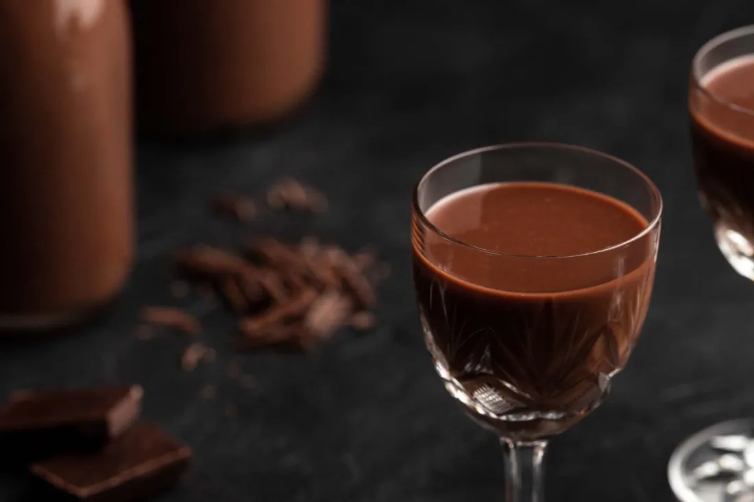 Schoko-Eierlikör mit Wodka und Amaretto in zwei Likörgläsern und zwei Flaschen auf einem dunklen Untergrund.