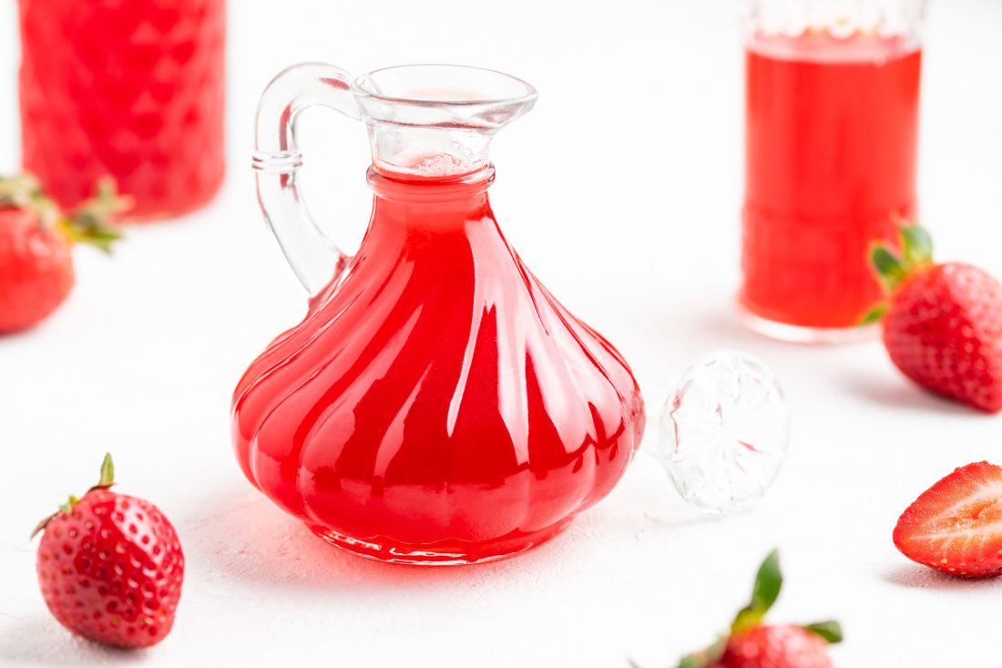 Drei Flaschen bzw. Gläser befüllt mit dem roten, fruchtigen Erdbeeressig.
