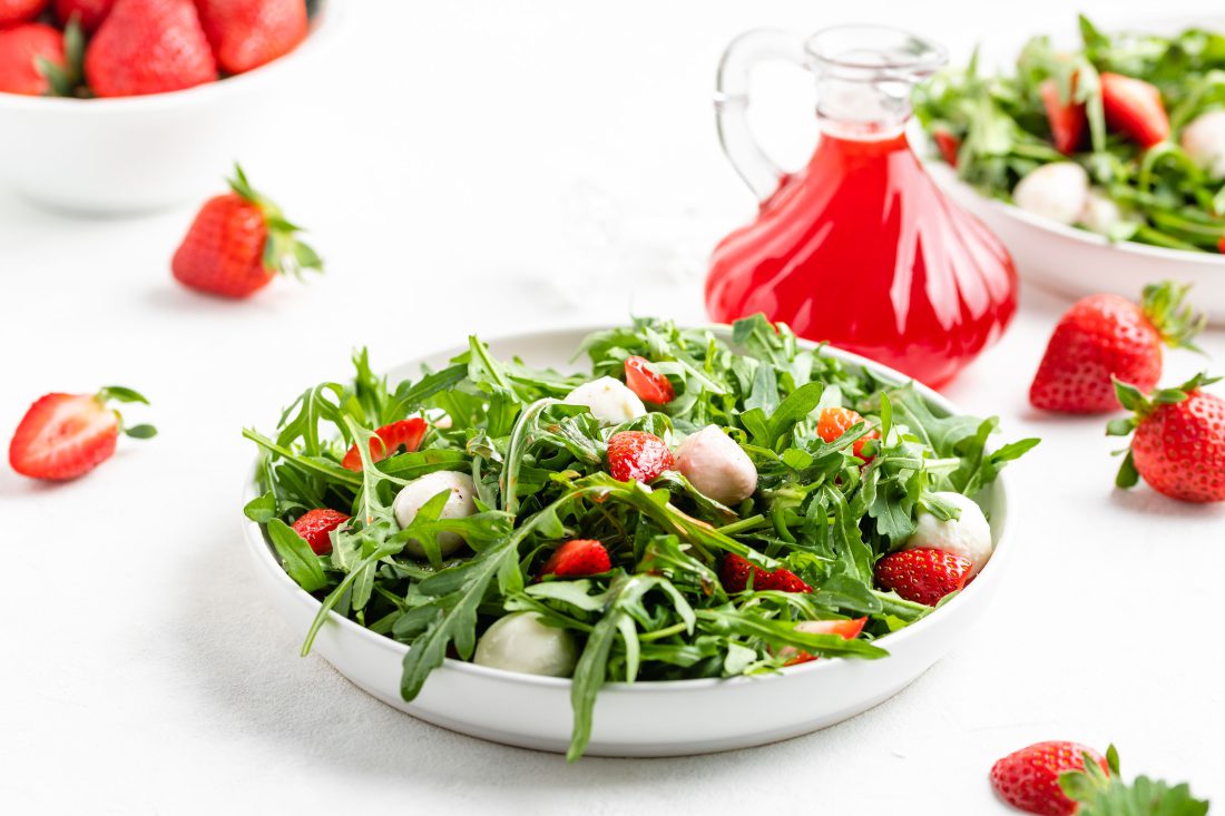 Salat mit Rucola, Erdbeeren und Mozzarella angerichtet auf einem weißen Teller und beträufelt mit dem selbstgemachten Erdbeeressig.