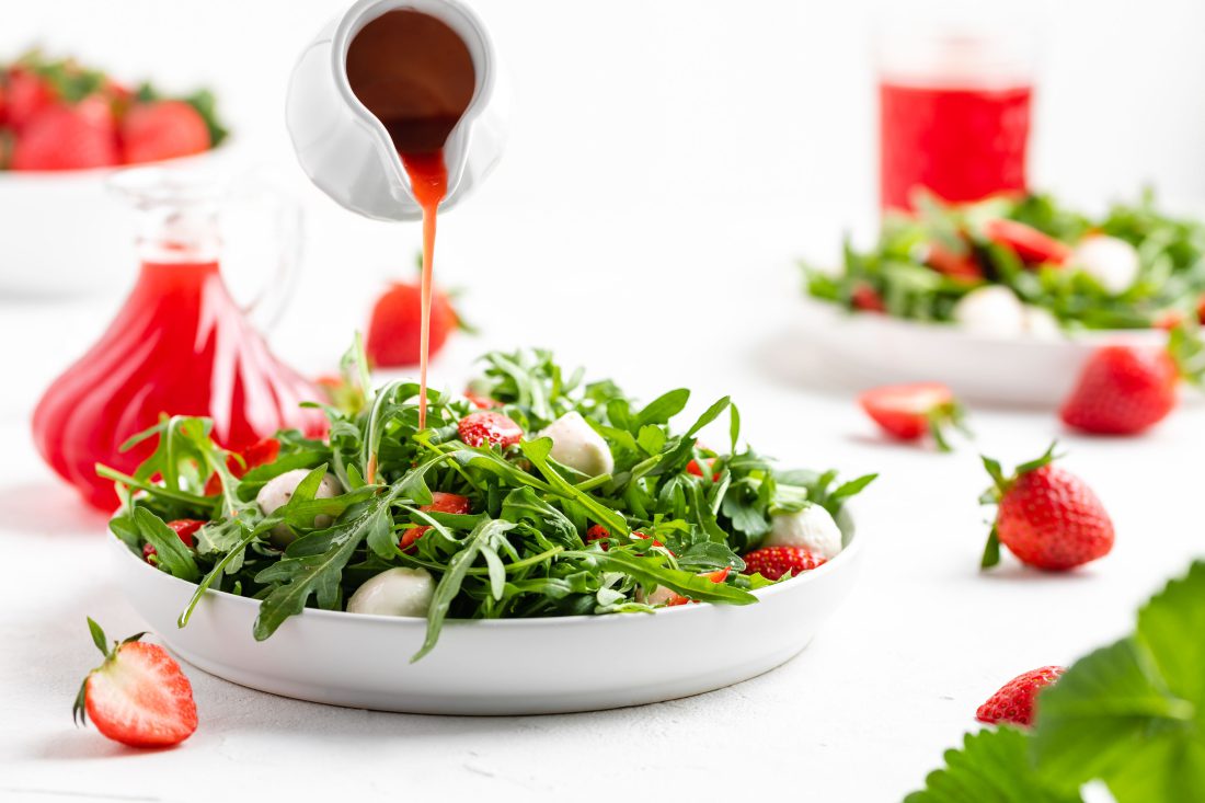 Der selbstgemachte Erdbeeressig wird gerade auf einem Salat aus Rucola, Erdbeeren und Mozzarella verteilt.