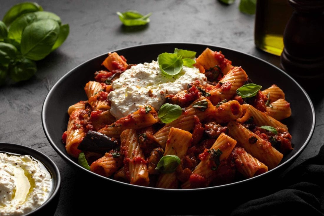 Sizilianische Pasta alla Norma angerichtet in einem tiefen Teller, garniert mit Chiliflocken und Basilikum.