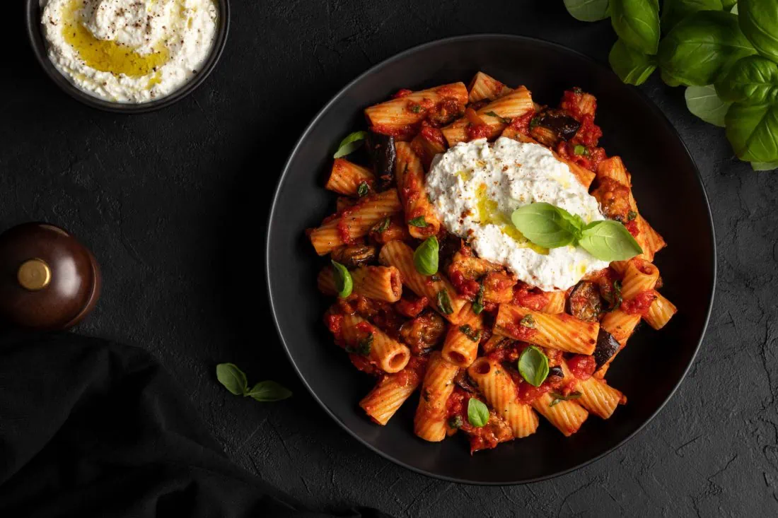 Sizilianische Pasta mit Ricotta und Auberginen in einem schwarzen Teller garniert mit Basilikumblättern.