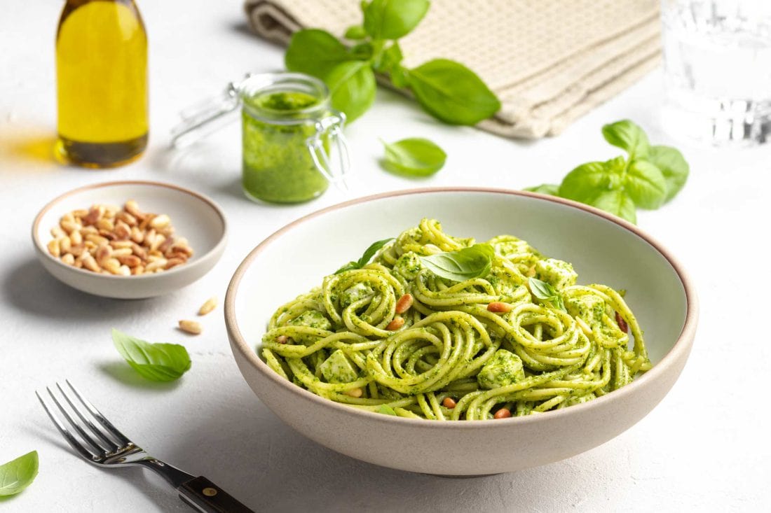 Spaghetti-Salat mit Pesto und Feta angerichtet auf einem weißen Tisch.