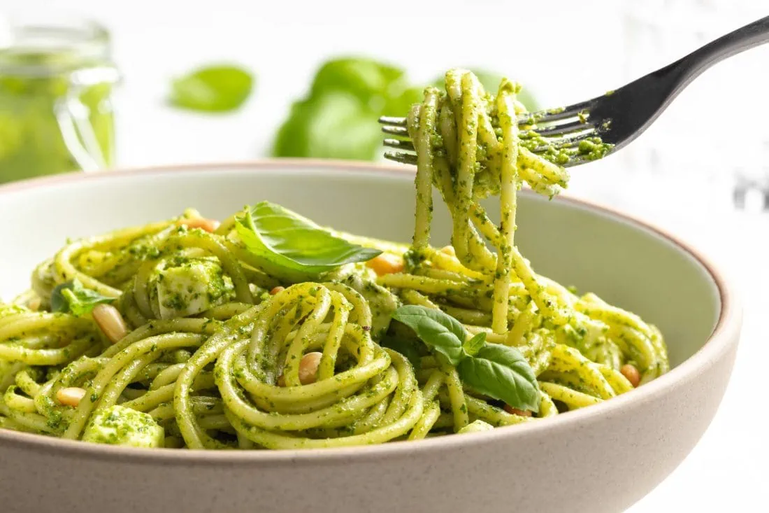 Spaghetti-Salat mit Pesto wird mit einer Gabel aus einem tiefen Teller gegessen.