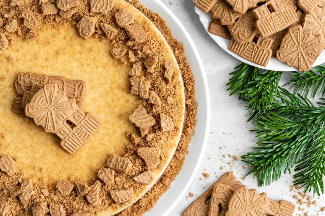 Spekulatius Cheesecake von Oben, neben mehreren Tannenzweigen, garniert mit Keksbröseln.