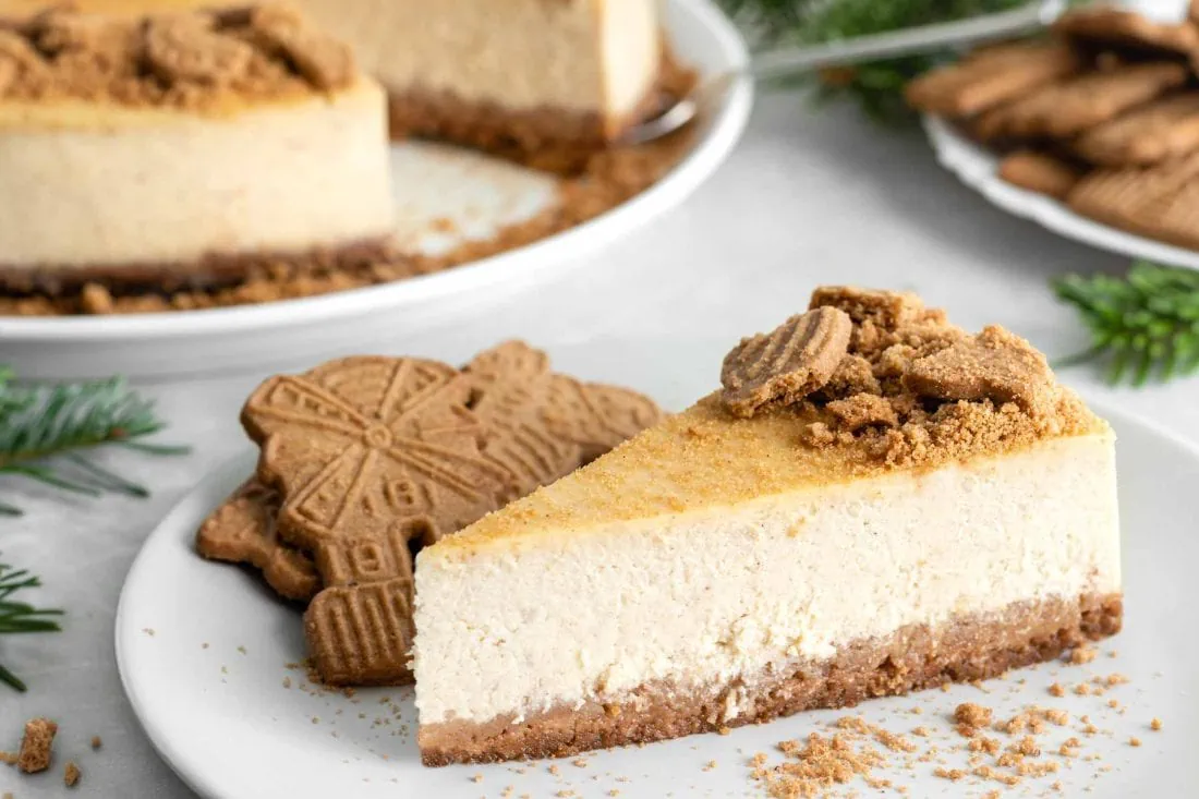 Spekulatius Cheesecake angeschnitten auf einem Teller mit Spekulatiuskeksen.