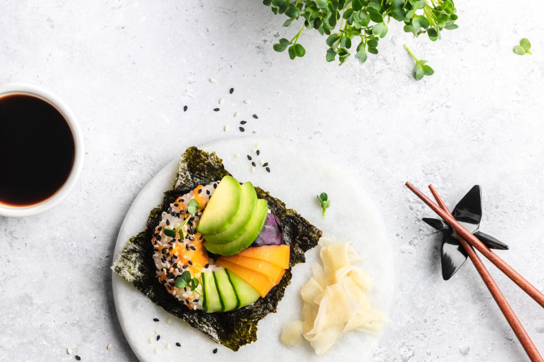 Sushi-Donut belegt mit Avocado, Gurke, Lachs, Rotkraut und Sesam auf einem Nori-Blatt.