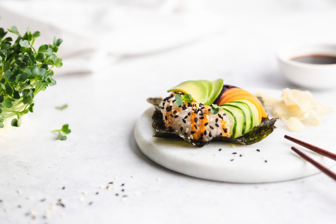 Ein Sushi Donut auf einem Algenblatt, belegt mit Avocado, Gurke, Lachs, Rotkohl und Sesam.