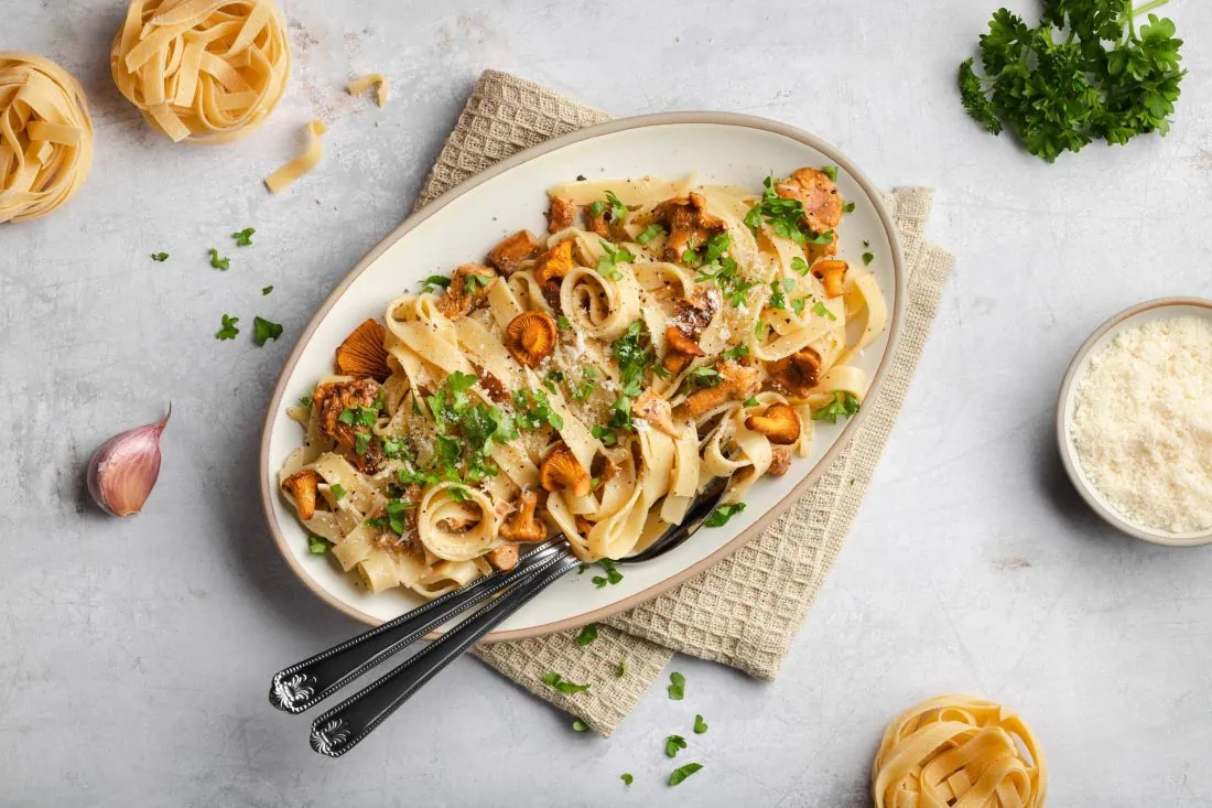 Bandnudeln mit frischen Pfifferlingen und Sahne serviert auf einem Teller mit geriebenem Parmesan und Petersilie.