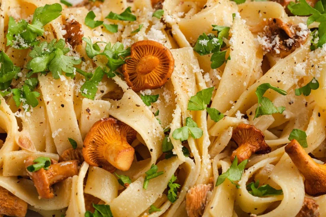 Nahaufnahmeder Tagliatelle mit frischen Pfifferlingen, garniert mit geriebenem Parmesan und gehackter Petersilie.