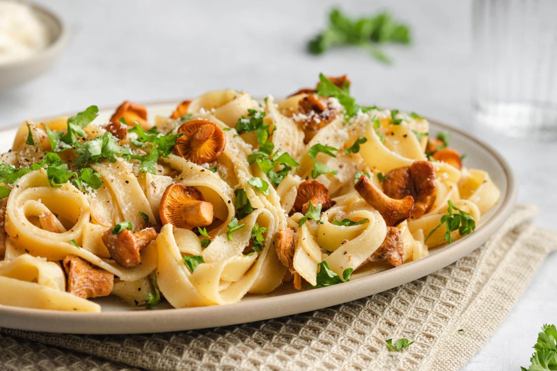 Eine Portion Pasta mit frischen Pfifferlingen und einer Sahnesauce serviert auf einem Teller.