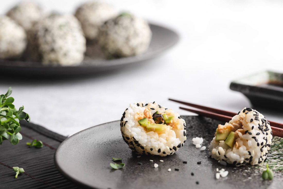 Ein halbiertes Sushi-Bällchen mit einer Füllung aus Gurke, Avocado und Thunfisch auf einem Teller.