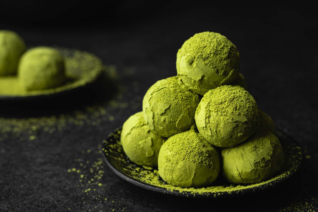 Vegane Matcha Energy Balls auf einem schwarzen Teller gestapelt voll mit grünem Matcha Pulver.