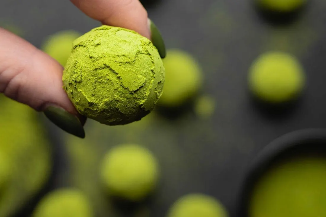 Veganer Matcha Energy Ball umhüllt mit grünem Matcha Pulver wird von zwei Fingern festgehalten.