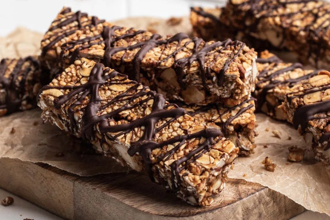 Vegane Schoko-Bananen Müsliriegel mit Haferflocken und Mandeln, verziert mit Zartbitterkuvertüre, liegen auf einem Backpapier.