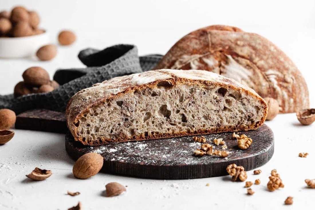 Ein in zwei Hälften geschnittenes Walnussbrot mit Dinkelmehl und Sauerteig liegt auf einem Holzbrett.