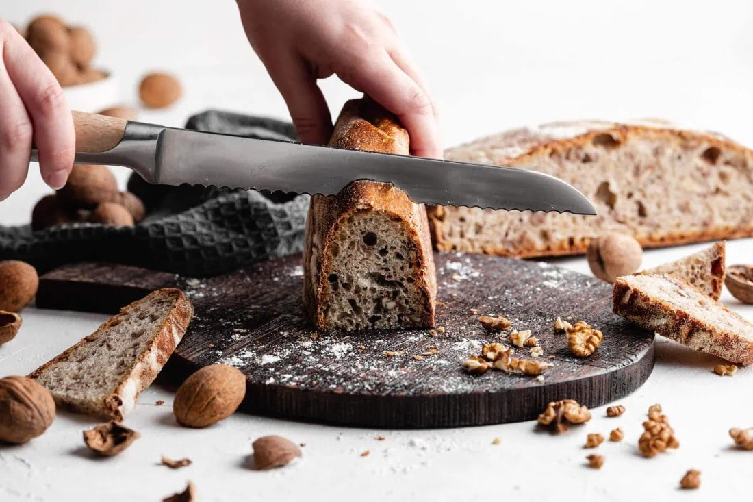 Das einfache Walnussbrot mit Dinkelmehl und Sauerteig wird mit einem Brotmesser in Scheiben geschnitten.