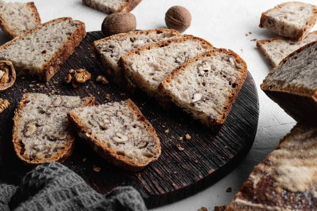 Walnussbrot aus Dinkelmehl in Scheiben geschnitten auf einem dunklen Holzbrett.