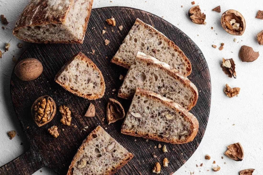 Einfaches Walnussbrot mit Dinkelmehl und Sauerteig aufgeschnitten auf einem Holzbrett. Daneben liegen Walnüsse.
