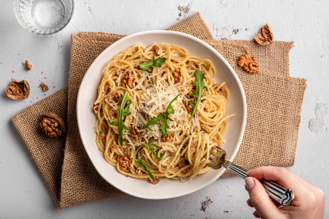 Italienisches Walnusspesto mit Parmesan serviert zu Spaghetti auf einem weißen Teller.