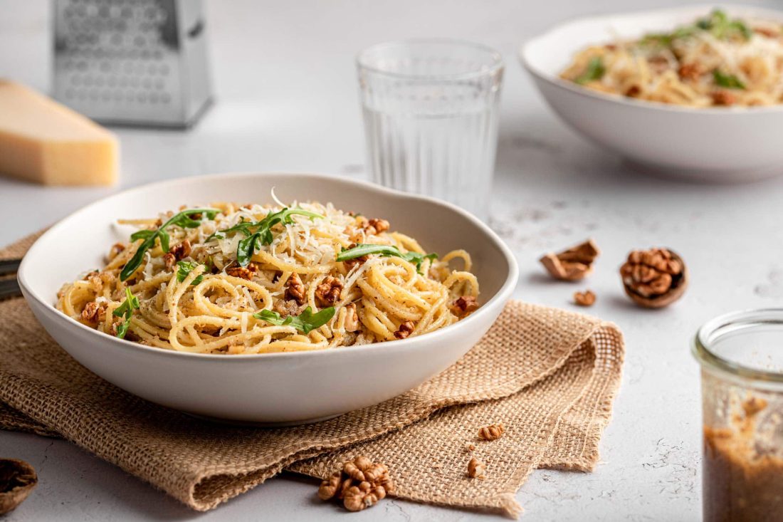 Italienisches Walnusspestos vermischt mit Spaghetti in tiefen Tellern. Die Nudeln mit Pesto sind mit frischem Parmesan bestreut.