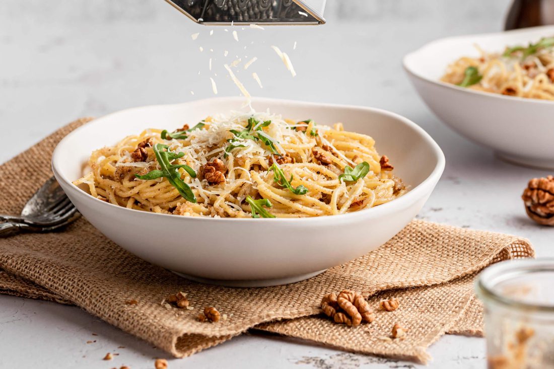Spaghetti mit Walnusspesto werden mit frisch geriebenem Parmesan bestreut.