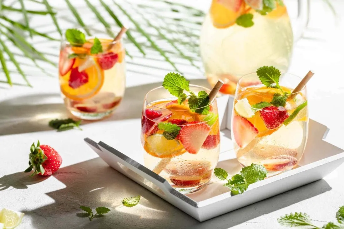 Spanische, weiße Sangria de Cava mit Sekt und Weißwein in Gläsern. In den Gläsern sind bunte Früchte und Zitronenmelisse.