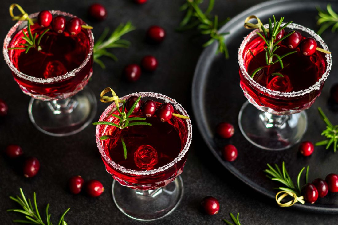 Wodka Cranberry Cocktails mit Rosmarin serviert in Champagnerschalen garniert mit frischen Cranberrys und einem Zuckerrand.
