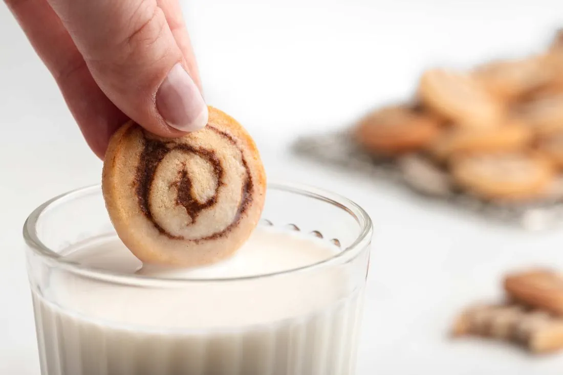 Ein Mini-Zimtschnecken Plätzchen wird in ein Glas mit Milch getunkt.