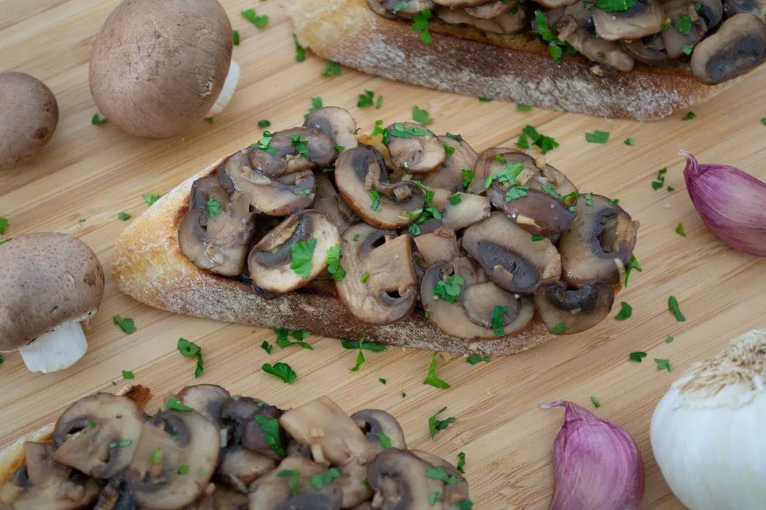 Geröstete Ciabatta-Scheiben, belegt mit gebratenen braunen Champignons, garniert mit frischer Petersilie