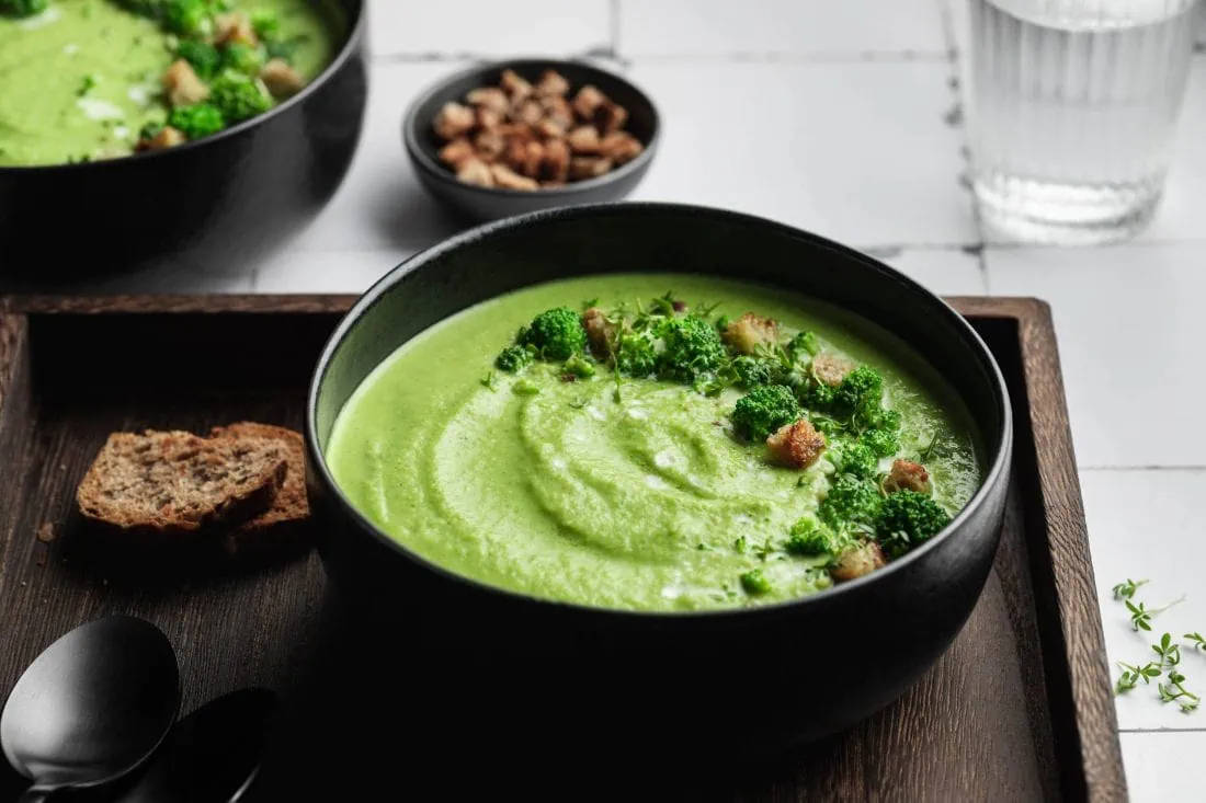 Schnelle Brokkolicremesuppe mit Croûtons, Brokkoli und Sahne garniert in schwarzen Schüsseln.